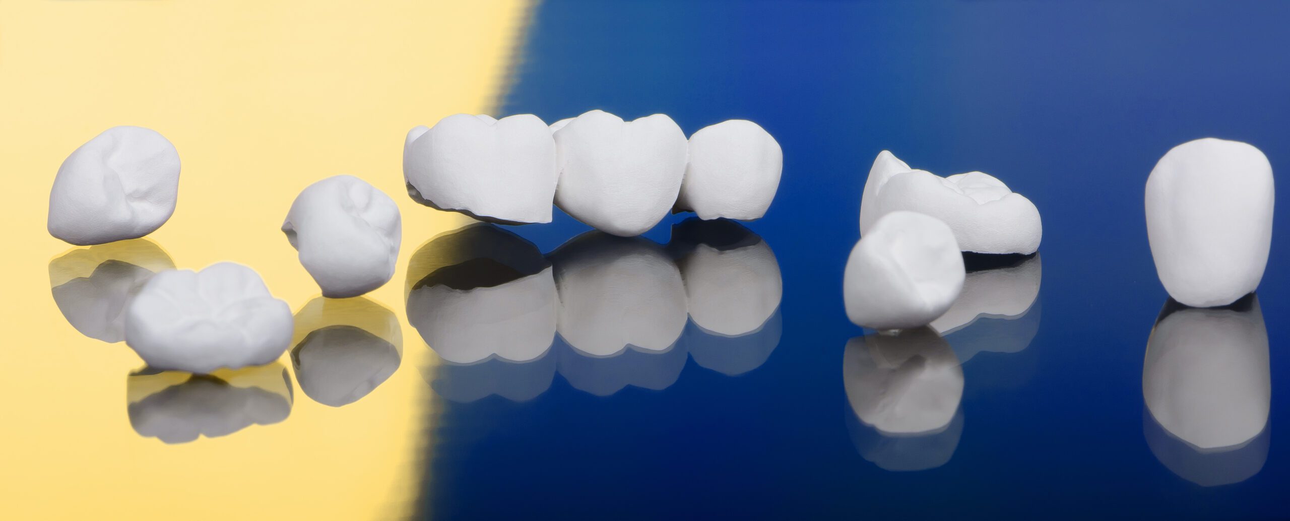 High aesthetic zirconia dentures and crowns on blue-yellow background. Top view on set of single dentures and dental crowns.